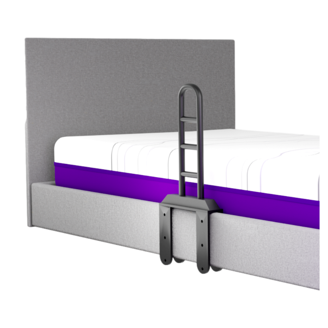 A gray upholstered bed with a tall headboard has an iCare Medical Bed Safety Rail attached on the side, providing sturdy bedside support. The mattress features a white top with a purple stripe along the edge.